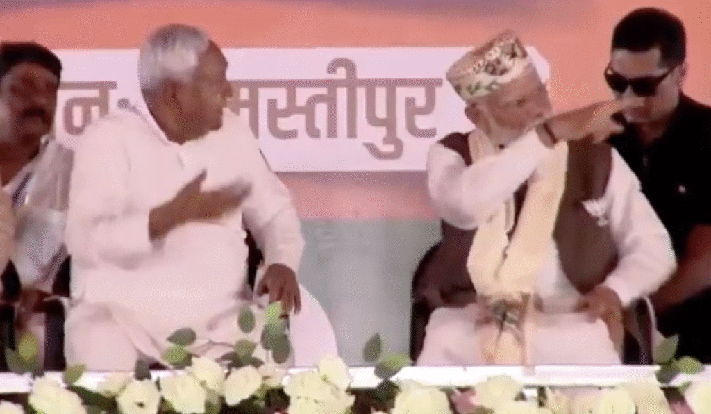 अनाउंसर की ओर नीतीश कुमार को भाषण के लिए बुलाने का इशारा करते पीएम मोदी।