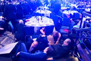 गोलीबारी के दौरान खुद को बचाने के लिए टेबिल के नीचे छुपने की कोशिश करते संवाददाता। (X/ JackPosobiec)